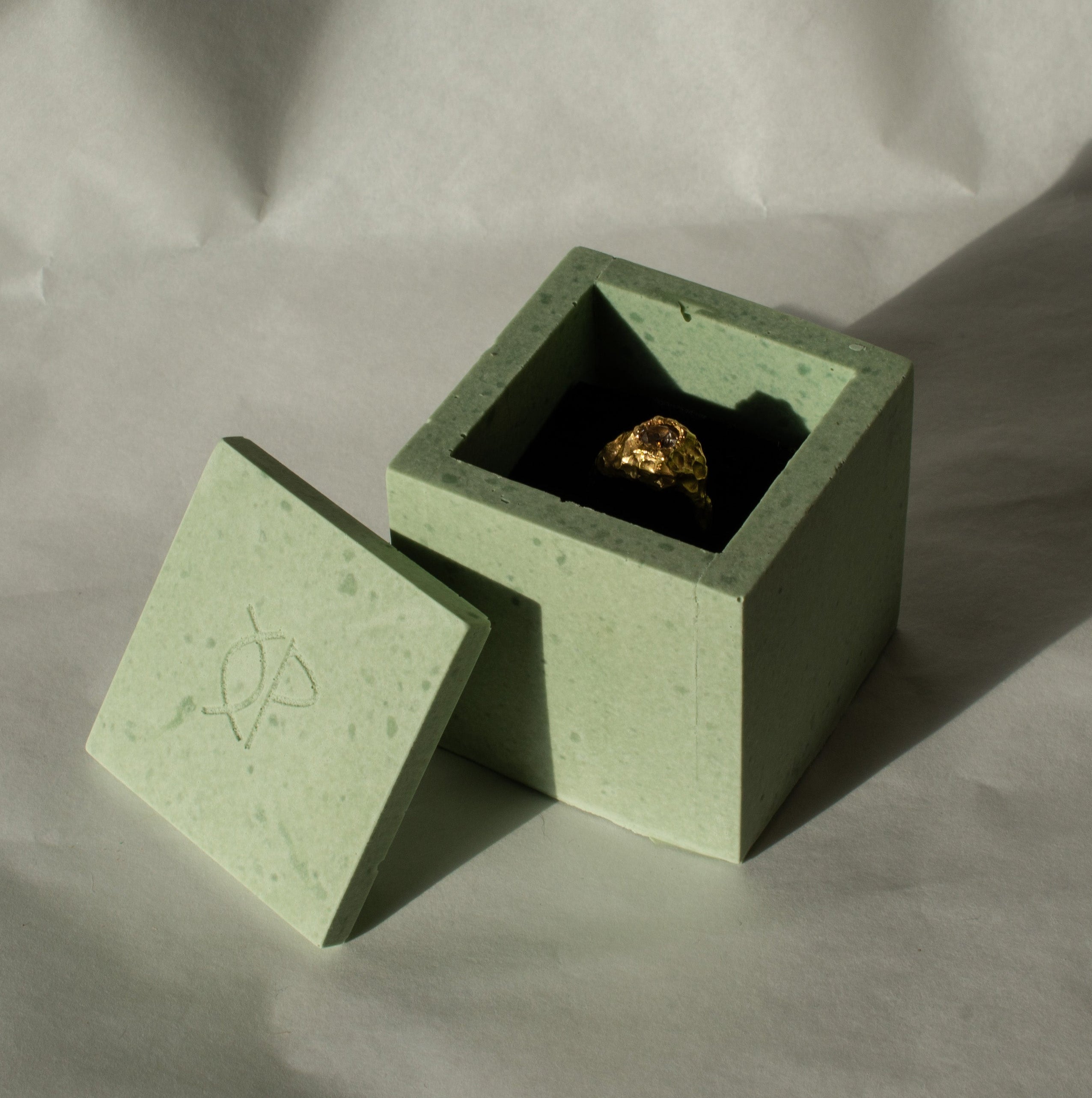 Green concrete box with a gold ring on a textured gray background